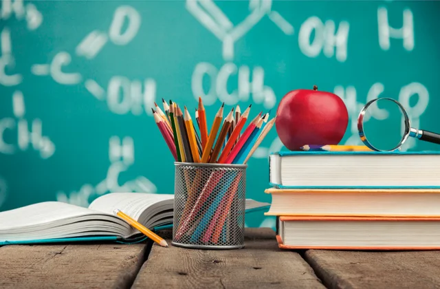 Imagem de mesa de professor com lápis e maçã e muitos livros.